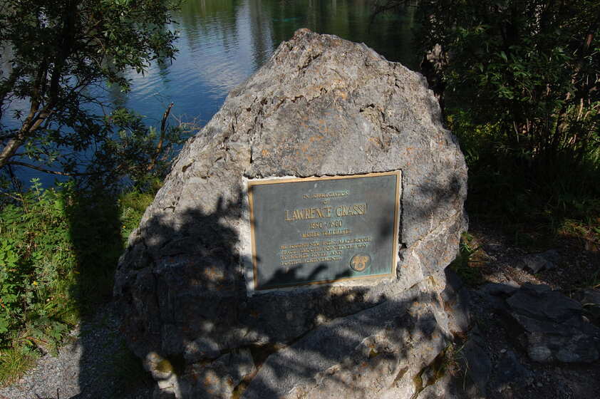 A rock with a plaque attached to it. The plaque reads: IN APPRECIATION OF LAWRENCE GRASSI 1890 - 1980 MASTER TRAILMAKER HE SOUGHT NEW PATHS, MADE ROUGH PLACES SMOOT, POINTED THE WAY TO HIGHER LEVELS AND LOFTIER ACHIEVEMENTS