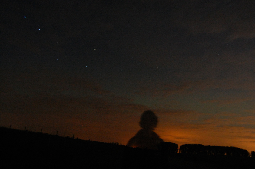 A silhouette of a person standing outdoors at night, with a starry sky and faint clouds in the background.