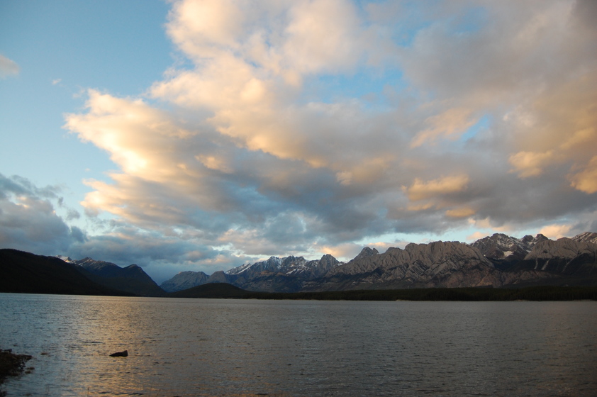 A calm lake at sunset, reflecting the colorful sky and silhouetted by mountains in the distance.