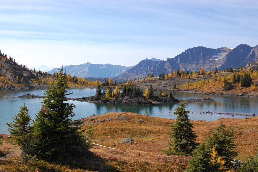 A serene alpine landscape with a clear blue lake surrounded by rugged mountains and autumn-colored trees.