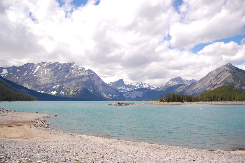 Mountain landscape with a serene lake nestled between towering peaks under a partly cloudy sky.