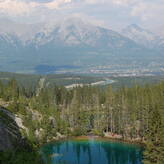 Several people are rock climbing on a cliff overlooking a valley with a river and forest. In the background, there are majestic mountains.
