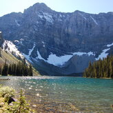 A scenic view of a lake surrounded by evergreen trees. The majestic peaks of the Canadian Rockies rise in the background.