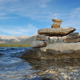 A pile of rocks juts out of the calm water of a mountain lake.