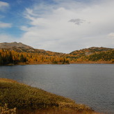 A still lake reflects the overcast sky, with trees lining the shore.