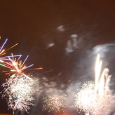 A group of fireworks exploding in a dark night sky. The fireworks are colorful and bright, with streaks of red, green, gold, and blue.