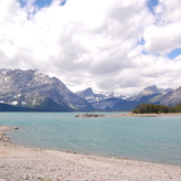 Mountain landscape with a serene lake nestled between towering peaks under a partly cloudy sky.