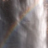 A waterfall with sunlight shining through, creating a rainbow effect in the mist.